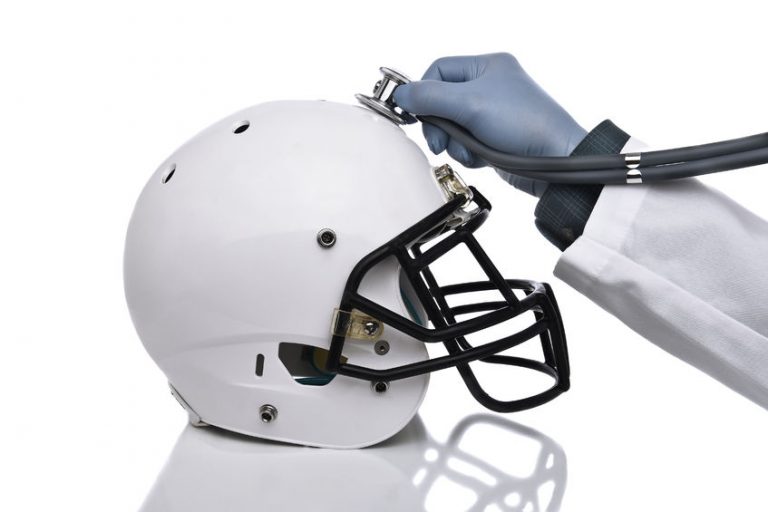 a football helmet and doctors hand holding a stethoscope on the crown of the helmet. sports concussion concept, and related conditions, cte, alzheimer's, parkinson's.
